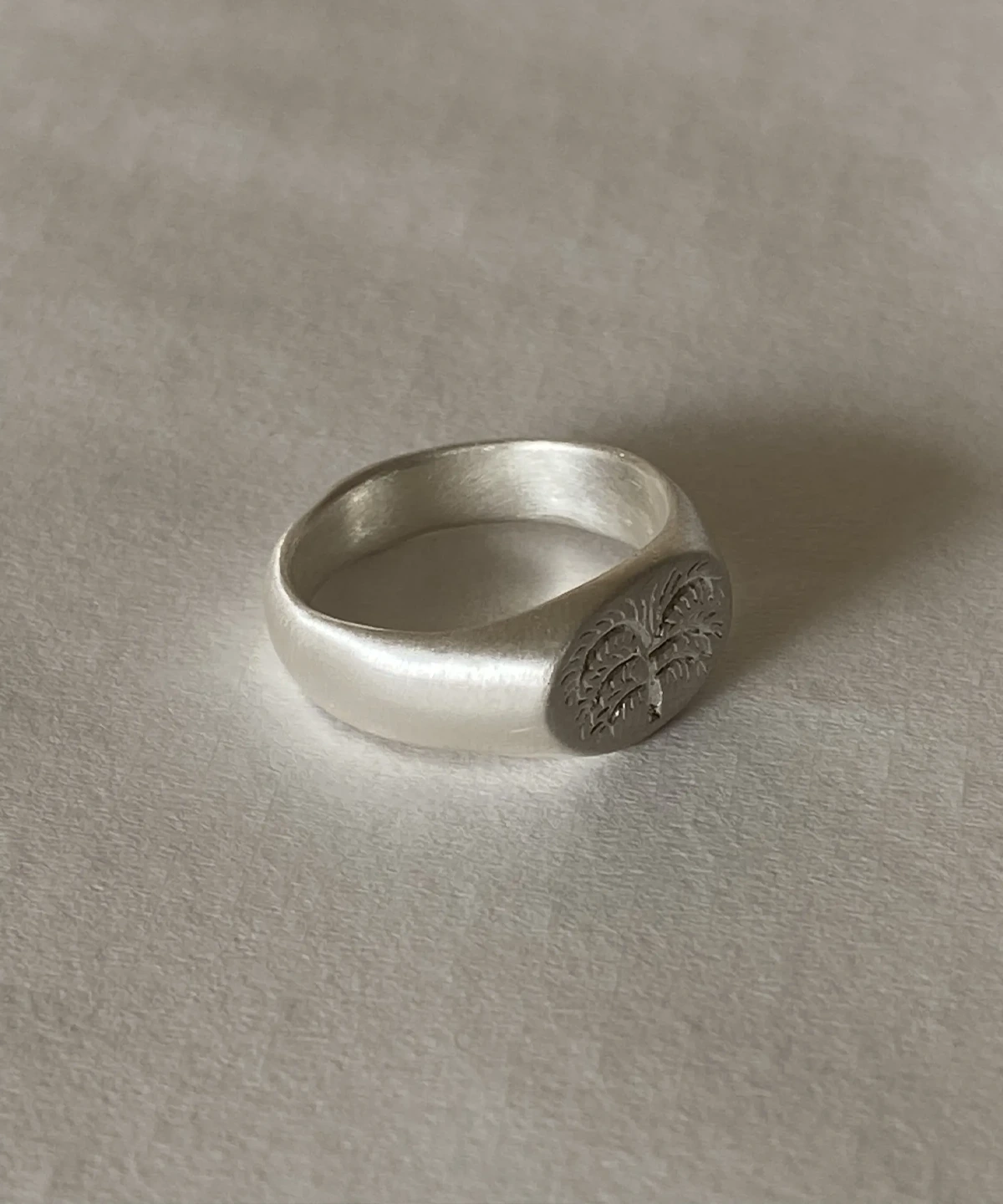 999 Silver Signet Ring with engraved organic tree design on matte circular face; handcrafted Silver Signet Ring placed on light textured surface, showcasing minimalist elegance and symbolic craftsmanship.