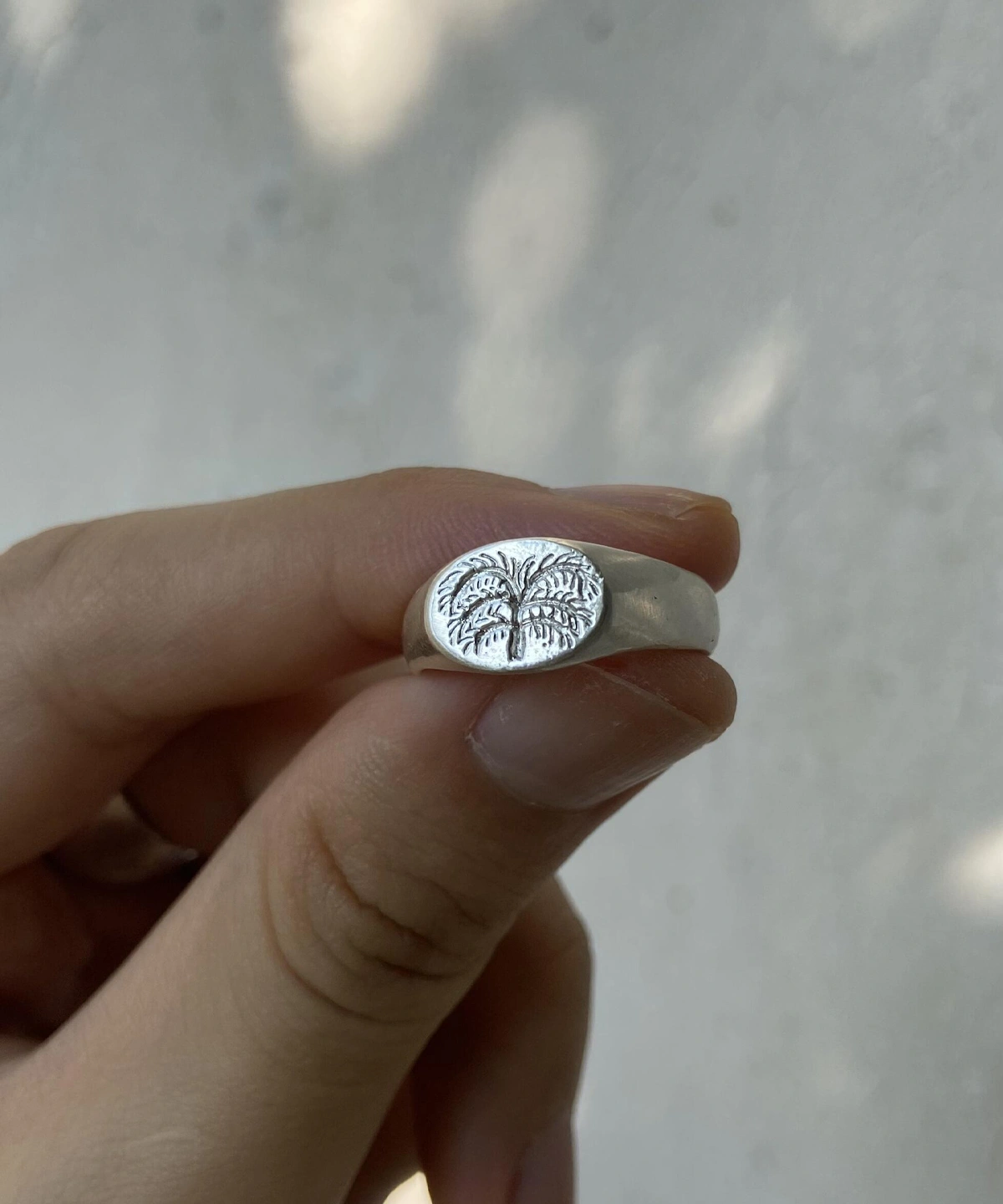 999 Silver Signet Ring with engraved palm tree design on oval face; handcrafted Silver Signet Ring held between fingers, styled against soft neutral background to highlight tropical symbolism and artisanal detail.