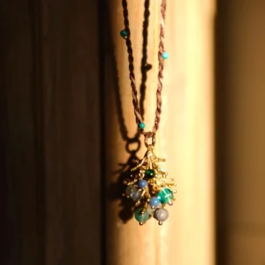 Juniper Berry-Turquoise Pinecone Necklace with twisted brown cord, turquoise beads, and gold-toned pinecone pendant; styled against warm wooden backdrop in sunlight to highlight handcrafted detail and forest-inspired elegance.