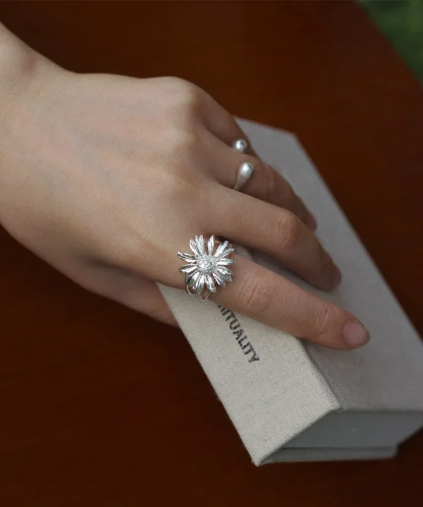 New In 29 A delicate silver daisy ring with detailed petals and a textured center, worn on the hand in soft natural light; a subtle April birth flower design.