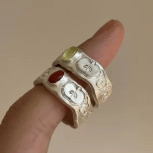 Two handcrafted silver rings with apple engravings and oval gemstones, including a green stone Natural Prehnite Ring, worn together on a finger.