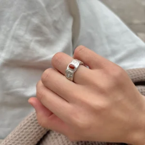 Natural Prehnite Ring in 999 Silver Green Apple Design 06 Silver ring with engraved apple motifs and a small oval red gemstone, worn on a hand against soft fabric textures.