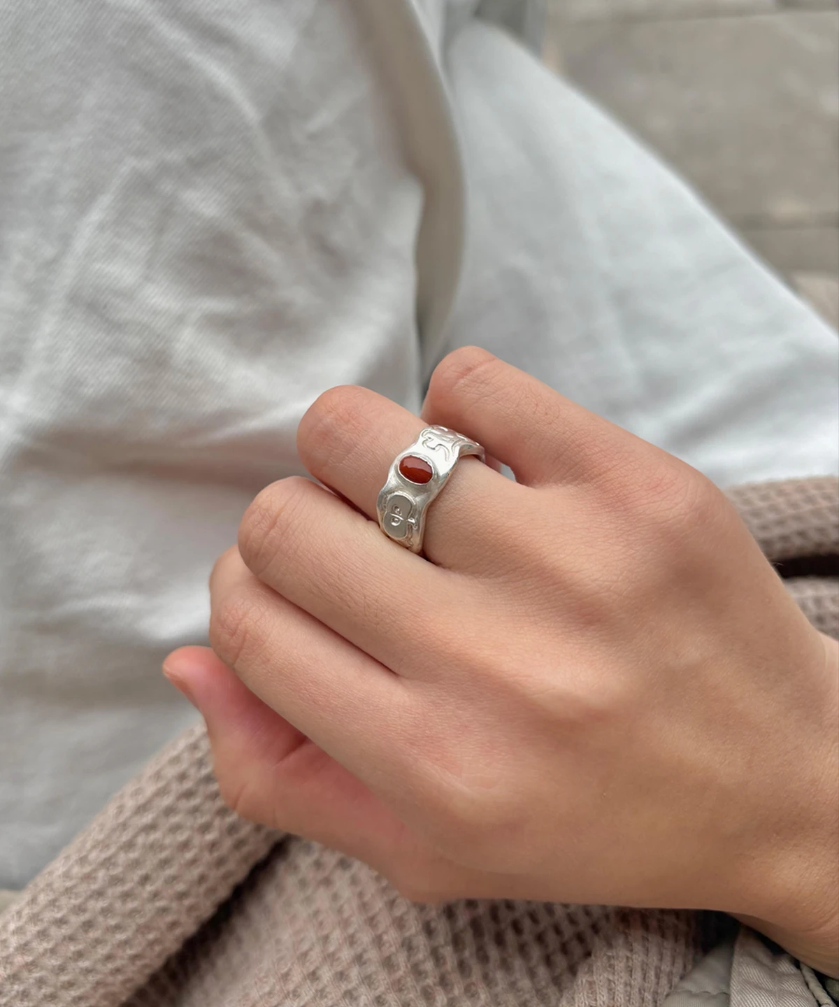 Natural Prehnite Ring in 999 Silver Green Apple Design 06 Silver ring with engraved apple motifs and a small oval red gemstone, worn on a hand against soft fabric textures.