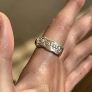 Natural Prehnite Ring in 999 Silver Green Apple Design 11 A handcrafted 999 silver band engraved with playful smiley faces and hearts, worn on the hand against soft fabric. A whimsical artisan detail styled alongside the Natural Prehnite Ring aesthetic.