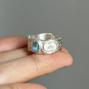 Natural Prehnite Ring in 999 Silver Green Apple Design 13 A handcrafted 999 silver ring featuring a blue oval aquamarine gemstone and engraved apple‑inspired symbols, held in hand to highlight the artisanal Natural Aquamarine Ring design.