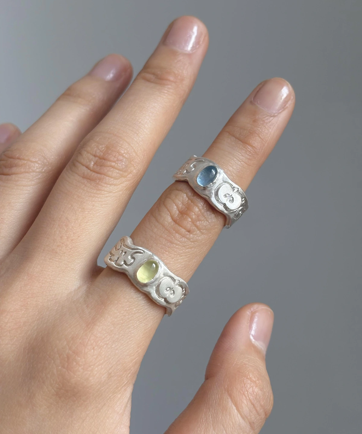 Natural Prehnite Ring in 999 Silver Green Apple Design 14 Two handcrafted 999 silver rings worn on the hand, each featuring an engraved apple motif and an oval gemstone. A playful artisan pairing styled to complement the Natural Prehnite Ring aesthetic.