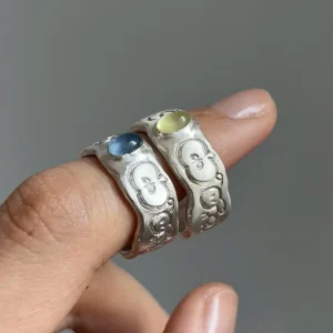 Natural Prehnite Ring in 999 Silver Green Apple Design 15 Two handcrafted 999 silver rings worn on adjacent fingers, each featuring an oval gemstone and embossed whimsical face motifs, styled to complement the Natural Prehnite Ring aesthetic.