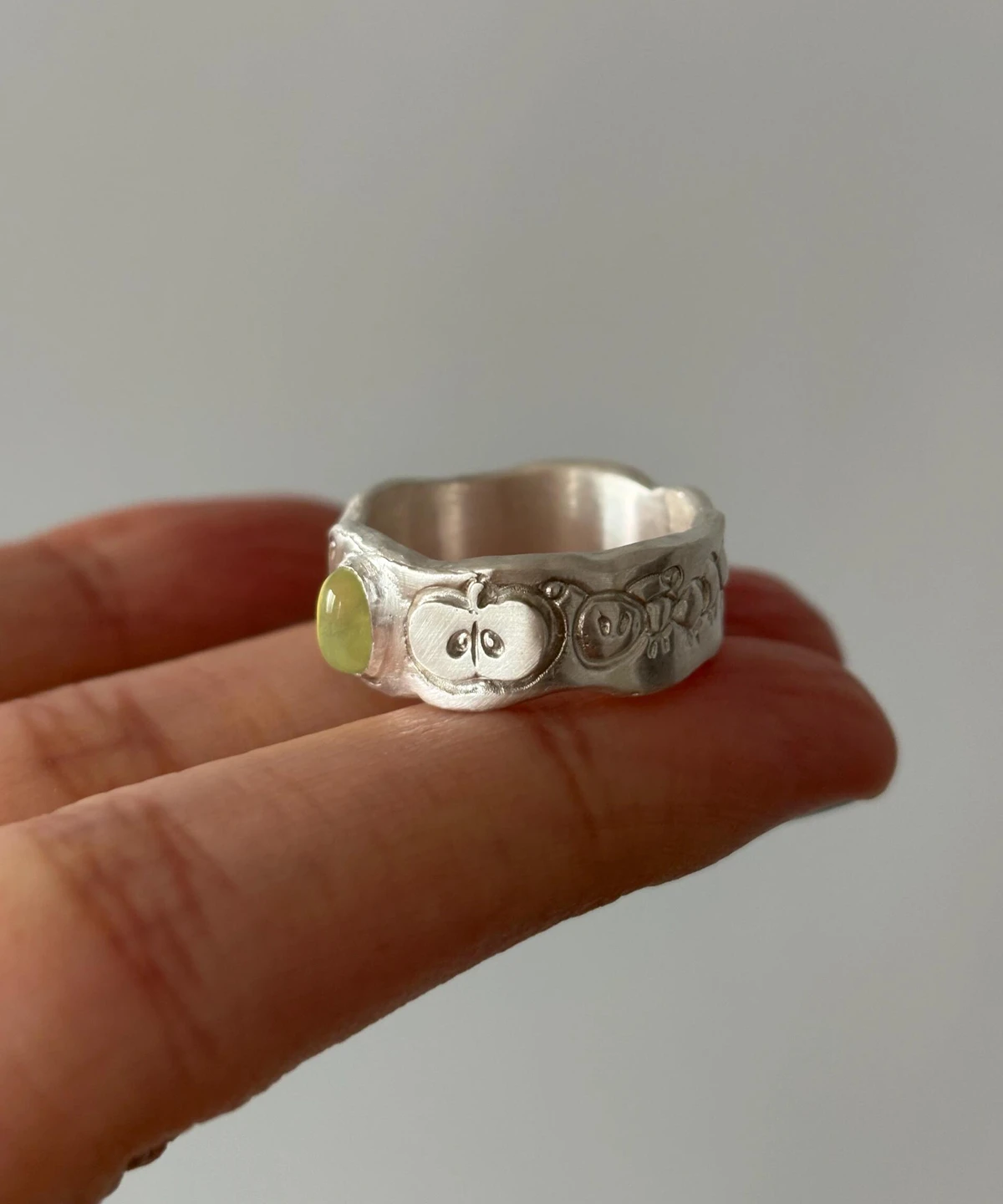 Natural Prehnite Ring in 999 Silver Green Apple Design 16 A handcrafted 999 silver ring with fruit‑inspired engravings and a light green gemstone, held in hand to highlight its artisanal texture and connection to the Natural Prehnite Ring style.