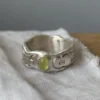 Home 32 A handcrafted 999 silver ring with an organic engraved band and a yellow‑green oval gemstone, displayed on textured white fabric, styled to complement the Natural Prehnite Ring aesthetic.