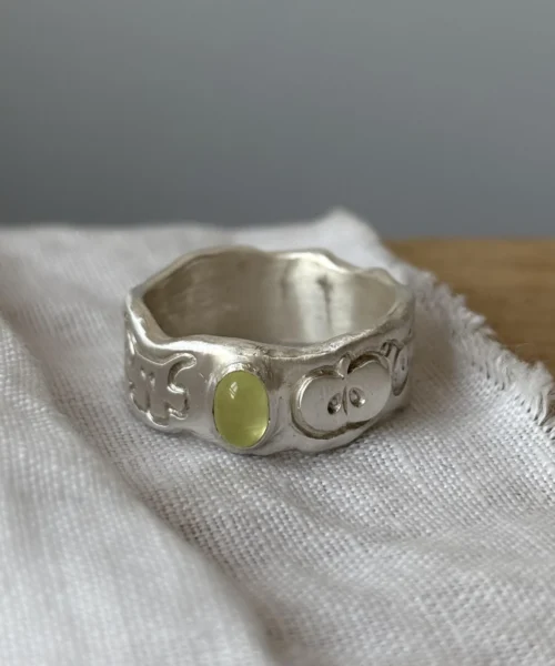 A handcrafted 999 silver ring with an organic engraved band and a yellow‑green oval gemstone, displayed on textured white fabric, styled to complement the Natural Prehnite Ring aesthetic.