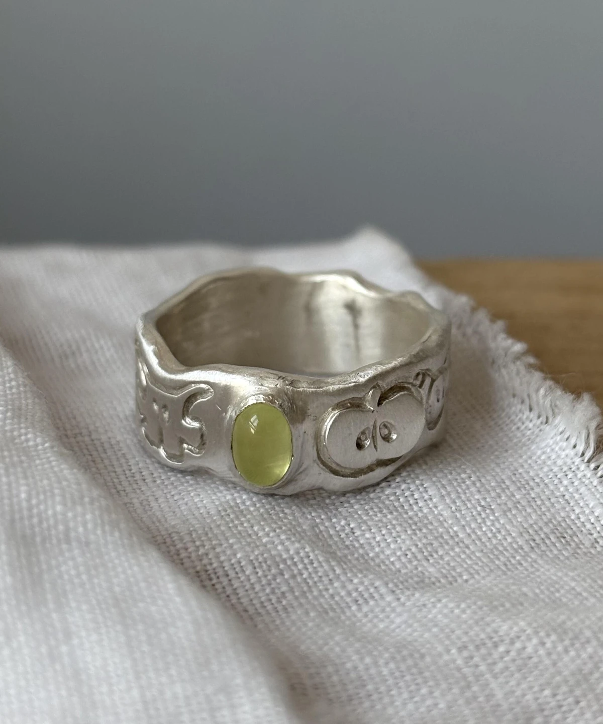 A handcrafted 999 silver ring with an organic engraved band and a yellow‑green oval gemstone, displayed on textured white fabric, styled to complement the Natural Prehnite Ring aesthetic.