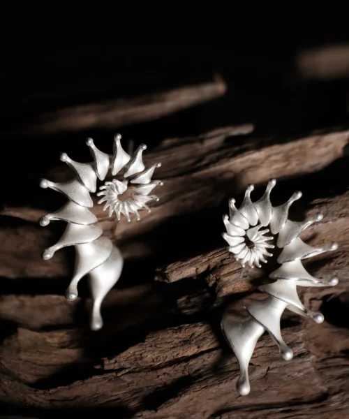A pair of Spiral Earrings crafted from S925 Sterling Silver, designed as ear cuffs with a unique spiral structure. The earrings feature smooth, flowing curves with tapered ends, resembling abstract organic forms. Their polished silver finish enhances their modern, artistic appeal. Displayed on a textured wooden surface, the intricate craftsmanship and elegant aesthetic of these Designer Ear Cuffs are emphasized.