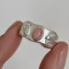 Home 39 Hand holding a handcrafted silver ring with a pink oval gemstone, featuring detailed ladybug and rabbit motifs on the band.