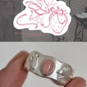 Hand holding a handcrafted silver ring with a pink oval stone, featuring engraved rabbit and strawberry motifs inspired by a whimsical Pink Opal Ring design.