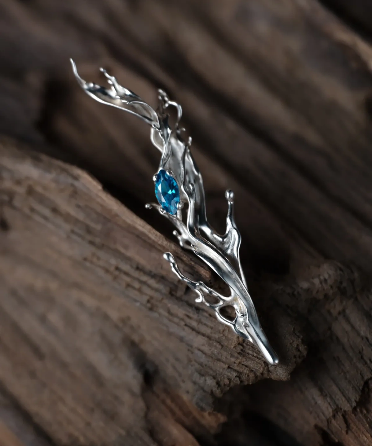 Tidewake Silver Earrings with fish-inspired flowing design and marquise-cut blue gemstone; placed on wood surface, featuring organic curves that evoke aquatic motion and handcrafted elegance in nature-themed Fish Earrings.