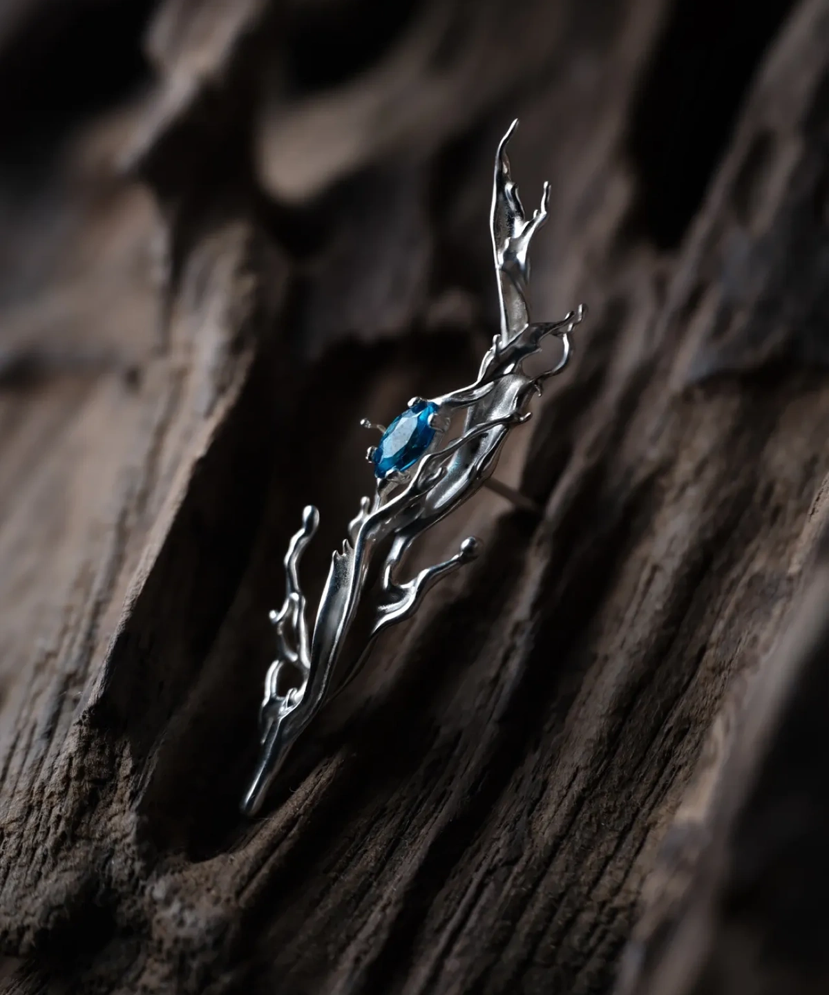 Tidewake Silver Earrings with fish-inspired sculptural design and blue gemstone; placed on wood surface, featuring organic flame-like curves and prong-set stone, highlighting aquatic elegance and handcrafted artistry in Fish Earrings.