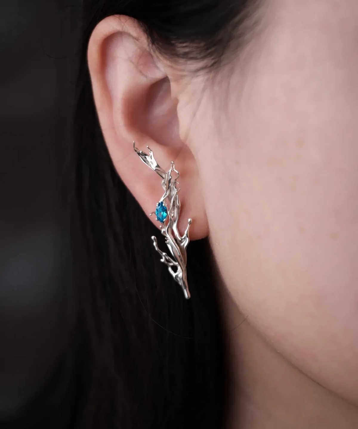 Tidewake Silver Earrings with fish-inspired branch design and blue gemstone; worn on ear, featuring organic structure that climbs along the ear contour, evoking aquatic elegance and handcrafted artistry.