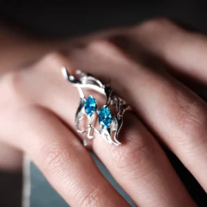 Sterling Silver Statement Ring with two vivid blue gemstones and flowing fishtail-inspired silverwork; handcrafted ring worn on hand, styled against blurred background to highlight sculptural elegance and gemstone brilliance.