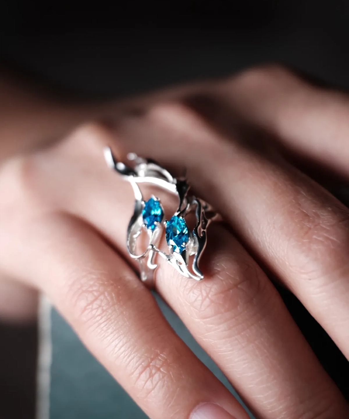 Sterling Silver Statement Ring with two vivid blue gemstones and flowing fishtail-inspired silverwork; handcrafted ring worn on hand, styled against blurred background to highlight sculptural elegance and gemstone brilliance.