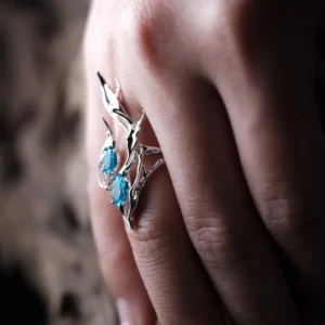 Sterling Silver Statement Ring with two oval blue gemstones and flowing fishtail-inspired silverwork; handcrafted ring worn on hand, styled against blurred background to highlight sculptural elegance and gemstone brilliance.