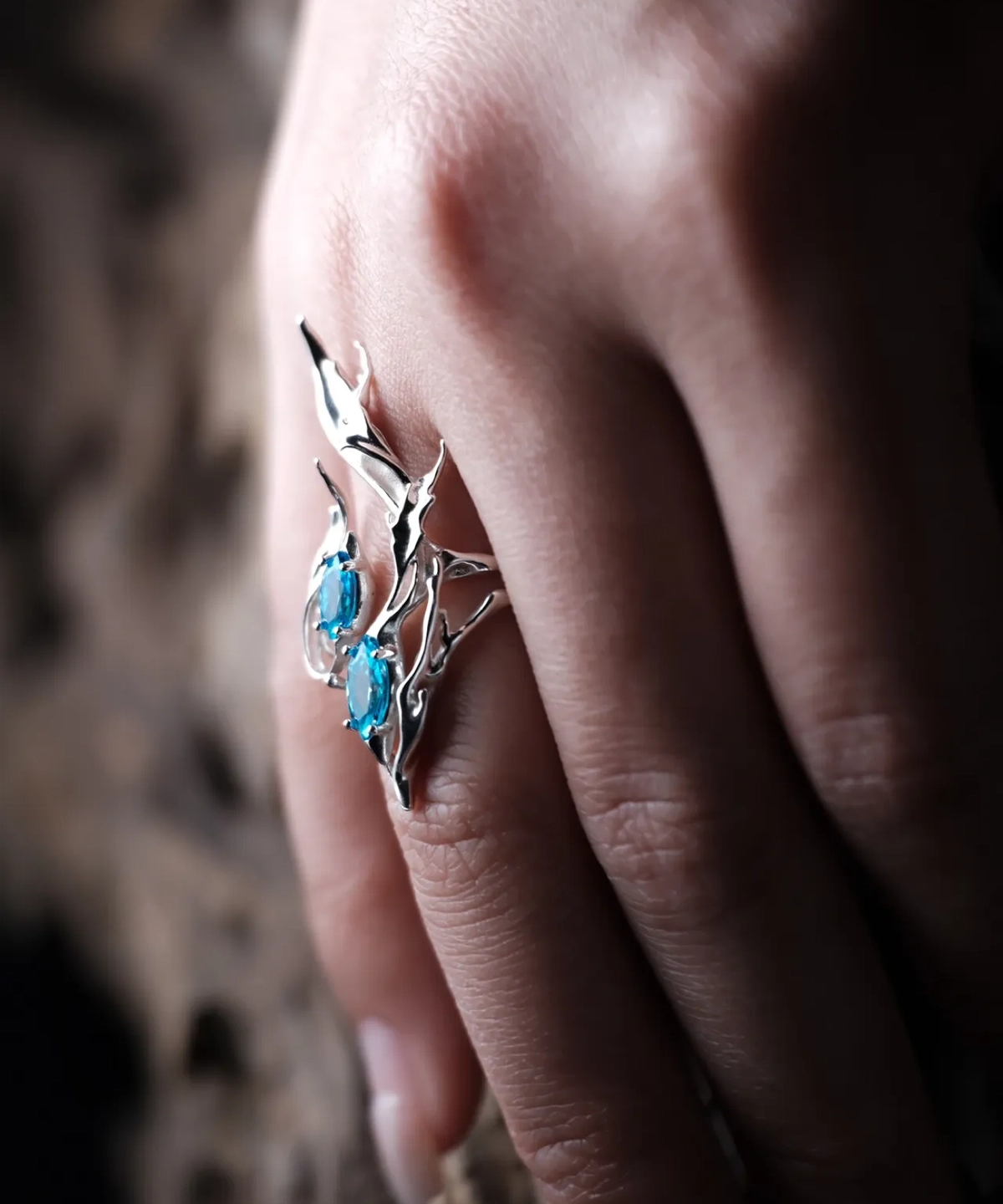 Sterling Silver Statement Ring with two oval blue gemstones and flowing fishtail-inspired silverwork; handcrafted ring worn on hand, styled against blurred background to highlight sculptural elegance and gemstone brilliance.