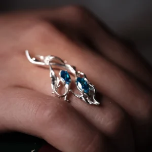 Sterling Silver Statement Ring with two marquise-cut blue gemstones and flowing fishtail-inspired silverwork; handcrafted ring worn on hand, styled against textured wood to highlight organic elegance and gemstone brilliance.
