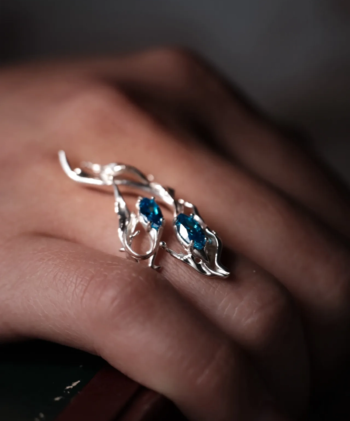 Sterling Silver Statement Ring with two marquise-cut blue gemstones and flowing fishtail-inspired silverwork; handcrafted ring worn on hand, styled against textured wood to highlight organic elegance and gemstone brilliance.