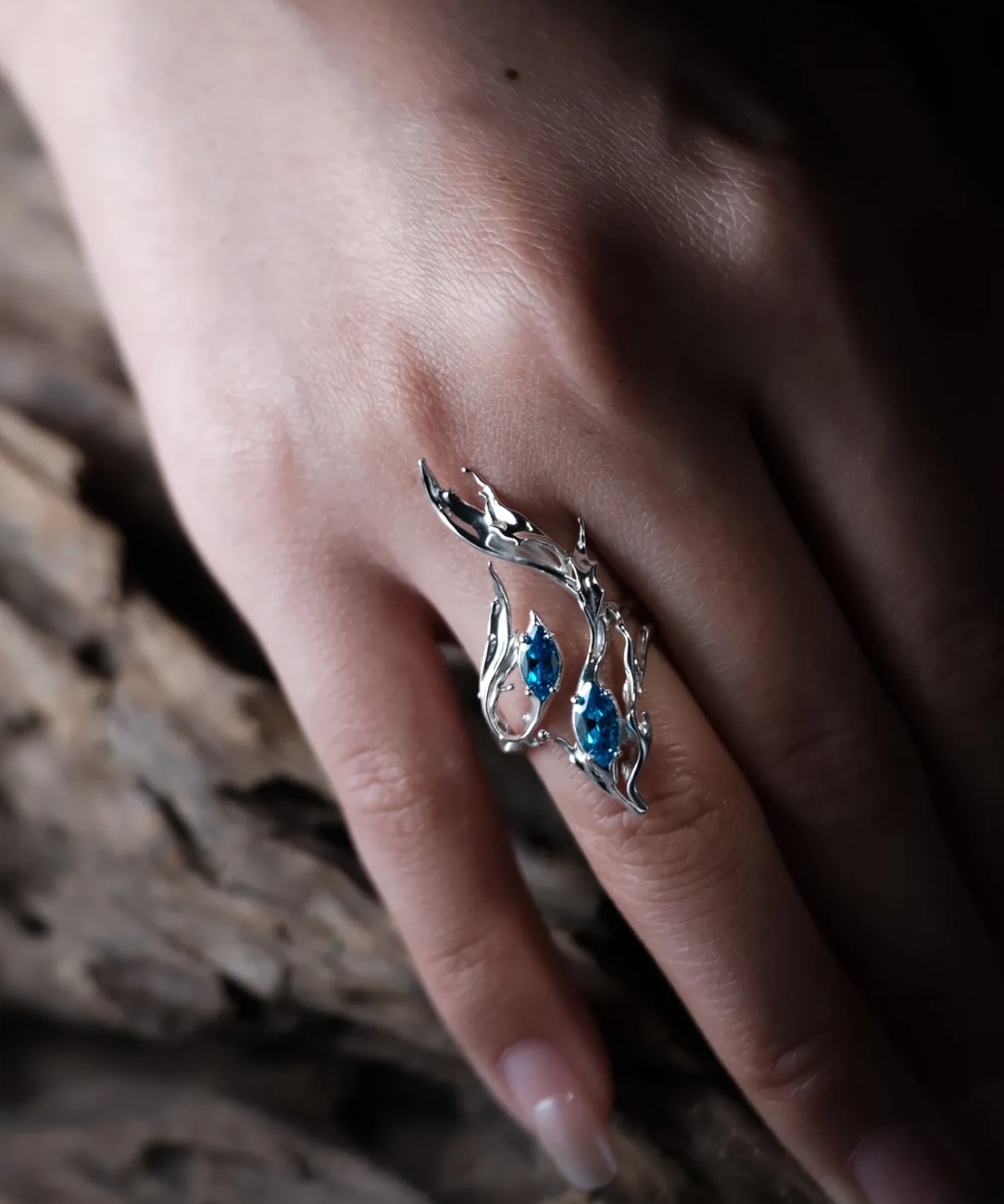 Sterling Silver Statement Ring with three marquise-cut blue gemstones and flowing fishtail-inspired silverwork; handcrafted ring worn on hand, styled against textured wood for natural contrast and artistic elegance.