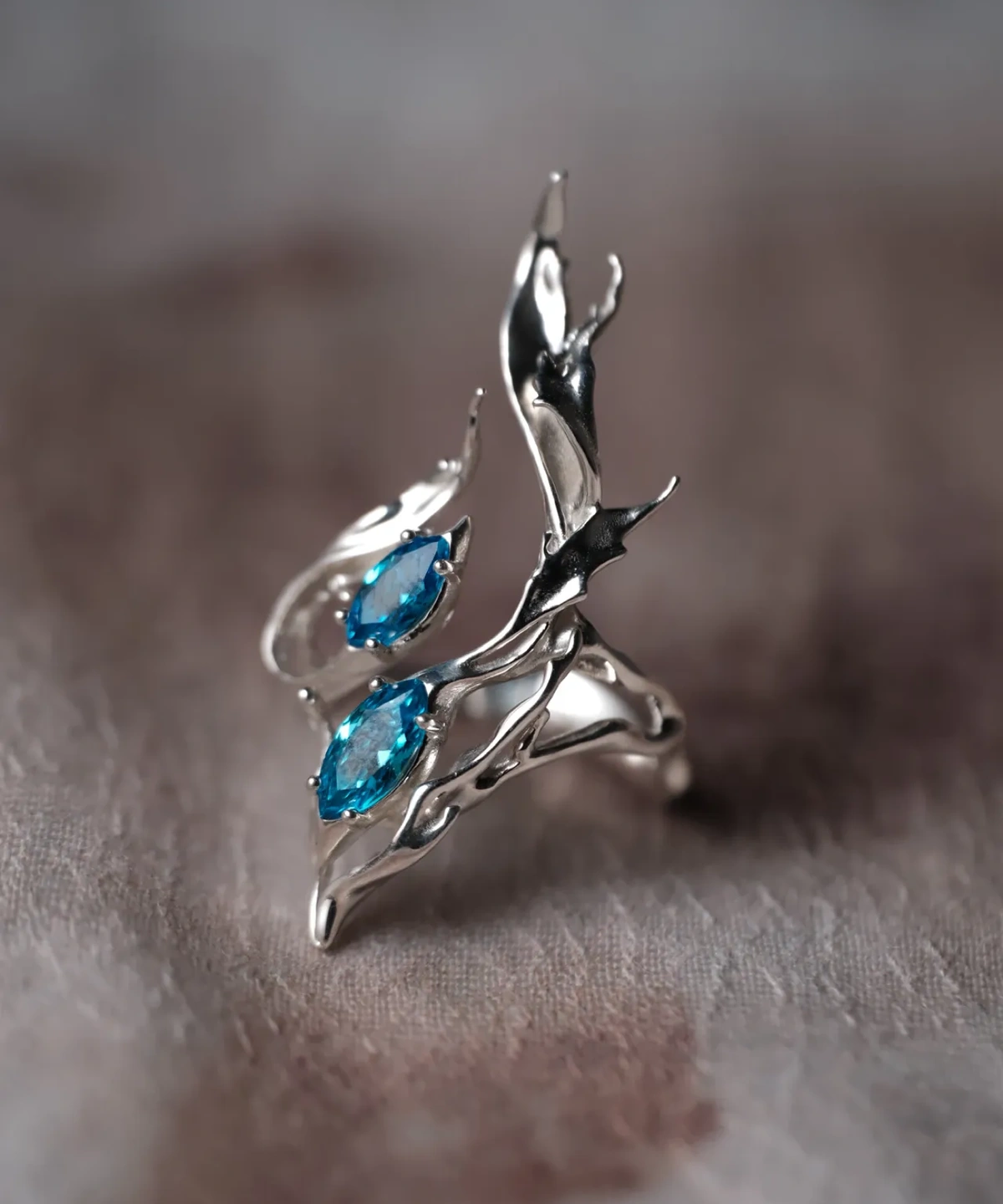 Sterling Silver Statement Ring with two marquise-cut blue gemstones and flowing fishtail-inspired silver curves; handcrafted ring held in hand, showcasing sculptural elegance and vibrant contrast.