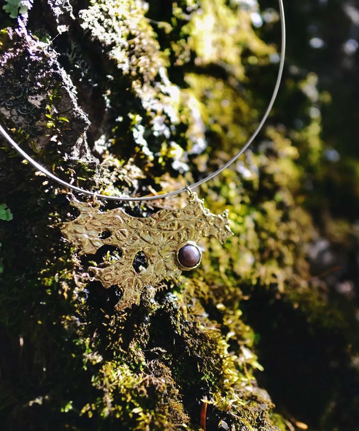 Tree Lichen Pendant on a silver choker necklace with natural agate; gold-toned organic pendant with embedded stone, styled against moss-covered rock to highlight forest-inspired craftsmanship and poetic botanical elegance.