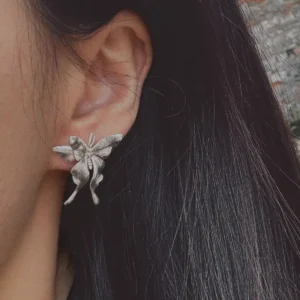 Asymmetric Butterfly Earrings in S990 sterling silver worn on the ear, featuring detailed sculpted wings and a delicate handcrafted look, framed by dark hair in a soft outdoor setting.