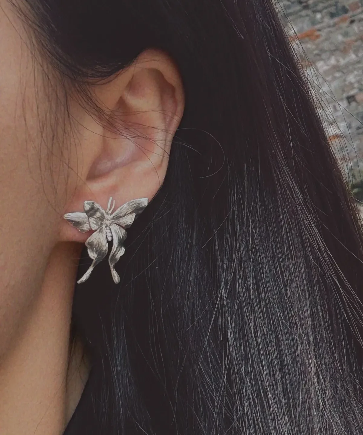 Asymmetric Butterfly Earrings in S990 Sterling Silver 03 Asymmetric Butterfly Earrings in S990 sterling silver worn on the ear, featuring detailed sculpted wings and a delicate handcrafted look, framed by dark hair in a soft outdoor setting.