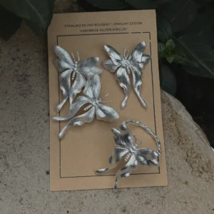 One handcrafted Butterfly Earrings and a Butterfly Ring in S990 sterling silver displayed on a brown card with green leaves, featuring sculpted wings and detailed textures in a natural setting.