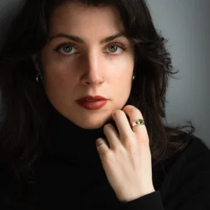 Hand wearing a silver August Birthstone Ring with a green gemstone, shown against green foliage and a dark background to highlight the Natural Peridot Ring design.