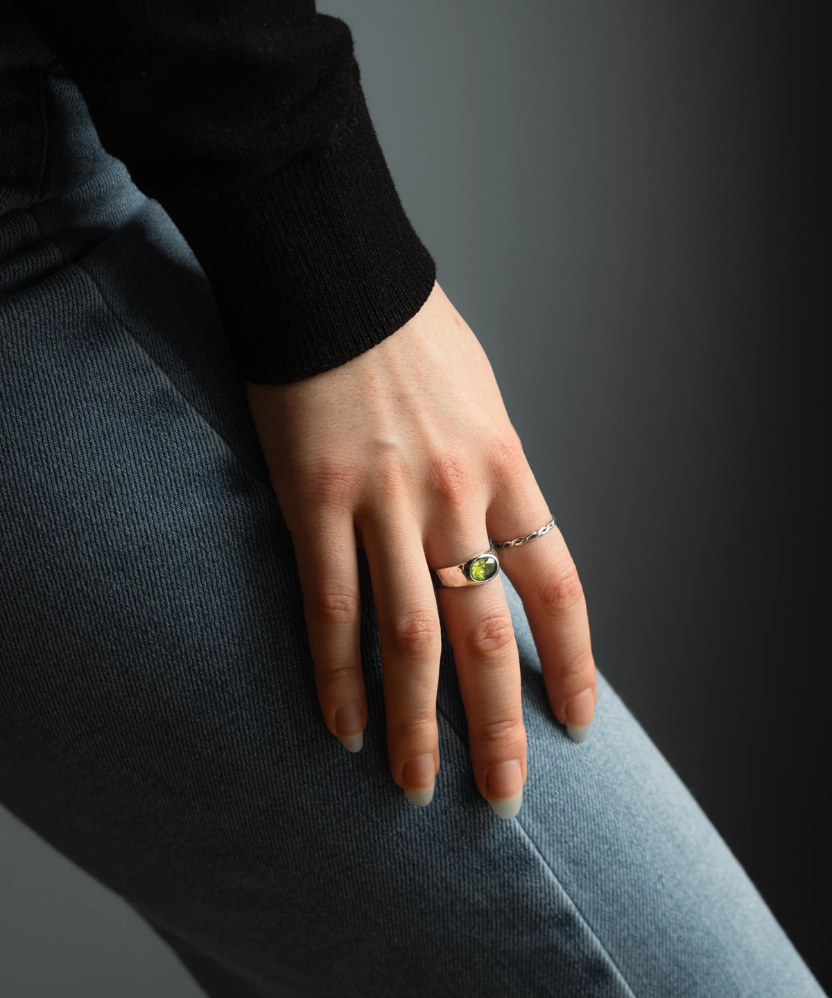 August Birthstone Ring-Natural Peridot Ring in Sterling Silver 11 Hand wearing a silver August Birthstone Ring with a vivid green gemstone, resting on denim and a black sleeve, highlighting the Natural Peridot Ring design.