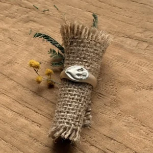 Flying Bird Ring-Handmade 999 Silver Signet Pinky Ring 03 Silver Signet Pinky Ring with a raised hand motif displayed on rolled burlap with small green leaves and yellow flowers on a wooden surface.