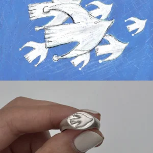 Silver Signet Pinky Ring with a raised bird‑inspired motif held between fingers, shown below matching bird artwork on a blue textured background.