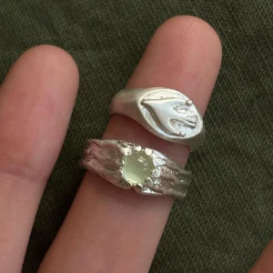 Flying Bird Ring-Handmade 999 Silver Signet Pinky Ring 10 Two silver Signet Pinky Rings worn on adjacent fingers, featuring a raised hand motif and an organic stone‑set design, shown against soft green fabric.