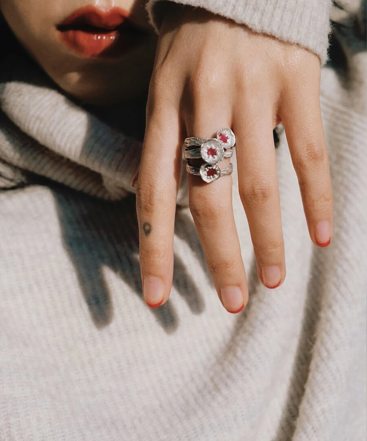 A handcrafted Poppy‑Inspired Ruby Ring in S925 sterling silver worn on the hand, featuring stacked rings with clear outer stones and red star‑shaped centers in a soft close‑up shot.