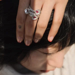 A handcrafted Poppy‑Inspired Ruby Ring in S925 sterling silver worn on the hand, featuring red gemstone floral designs stacked together in an artistic close‑up composition.
