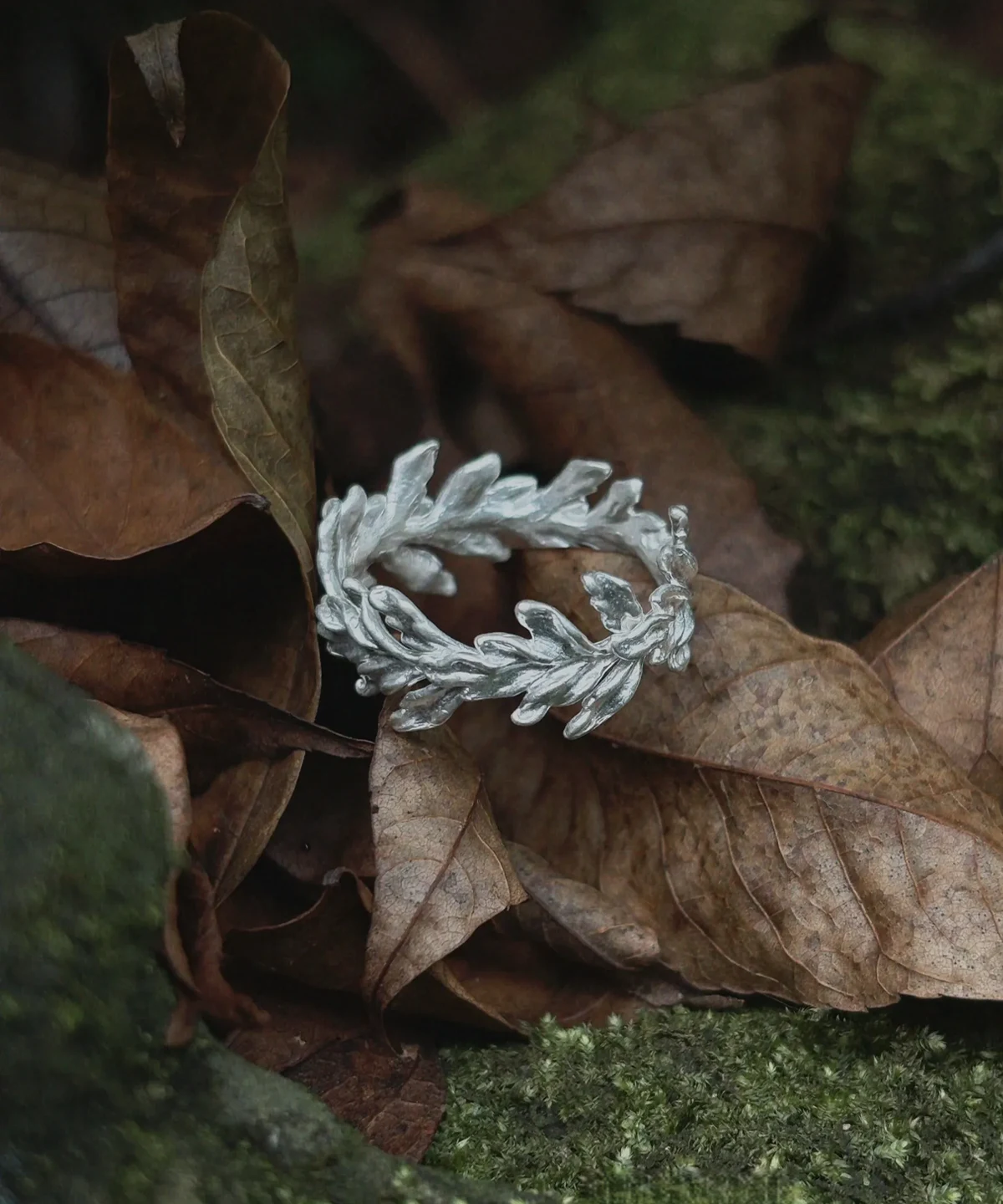 Silver Leaf Ring Jewelry with intertwined leaf motifs placed on dried leaves and mossy rocks, highlighting its botanical texture and nature‑inspired design.