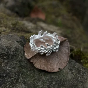 S925 Sterling Silver Poppy Leaf Ring Jewelry 06 Silver Leaf Ring Jewelry with intertwined leaf motifs resting on a dried leaf over a rock, highlighted by natural moss and earthy textures.