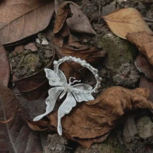 A handcrafted S990 Sterling Silver Butterfly Ring resting on soil and dried leaves, featuring detailed wings and a textured band that highlights its organic, nature‑inspired design.