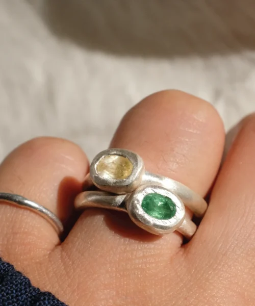Close-up of two handmade S925 sterling silver tourmaline rings with yellow and green gemstones, worn on a hand against a soft white fabric background