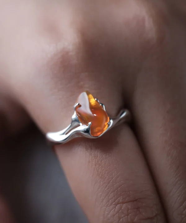 Close-up of a hand wearing a delicate Custom Gemstone Ring in polished sterling silver, featuring a warm teardrop-shaped orange fire opal in a fluid organic setting.