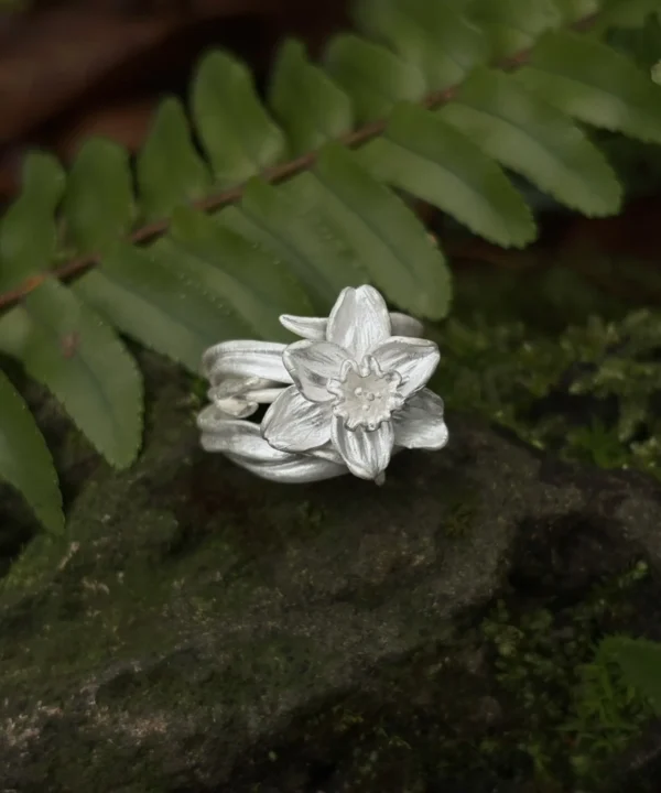 New In 12 Handmade S925 sterling silver Daffodil Ring with intricate flower details, displayed on a mossy rock against lush green fern foliage.