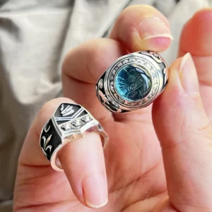 A hand holding two Vongola Ring replicas from Katekyo Hitman Reborn! in sterling silver, including one with a blue gemstone.