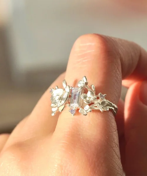 A close-up of a hand wearing the Unique Gemstone Ring, an orchid-inspired S925 silver ring with a central clear rectangular gemstone.