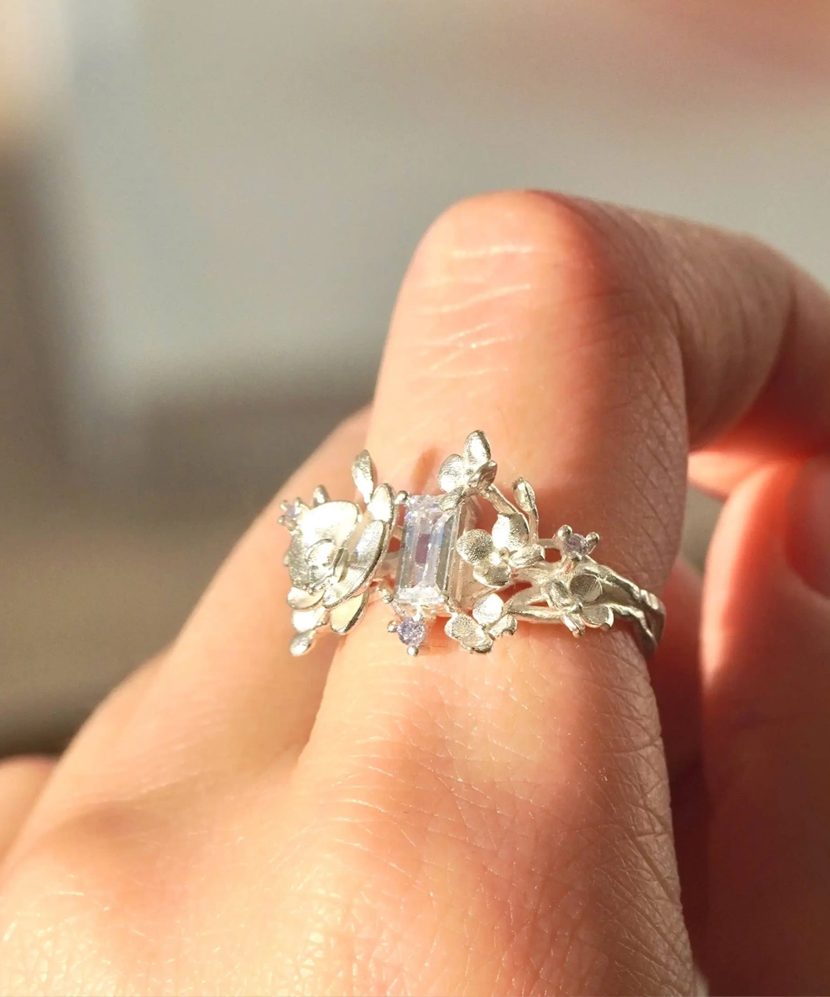 A close-up of a hand wearing the Unique Gemstone Ring, an orchid-inspired S925 silver ring with a central clear rectangular gemstone.