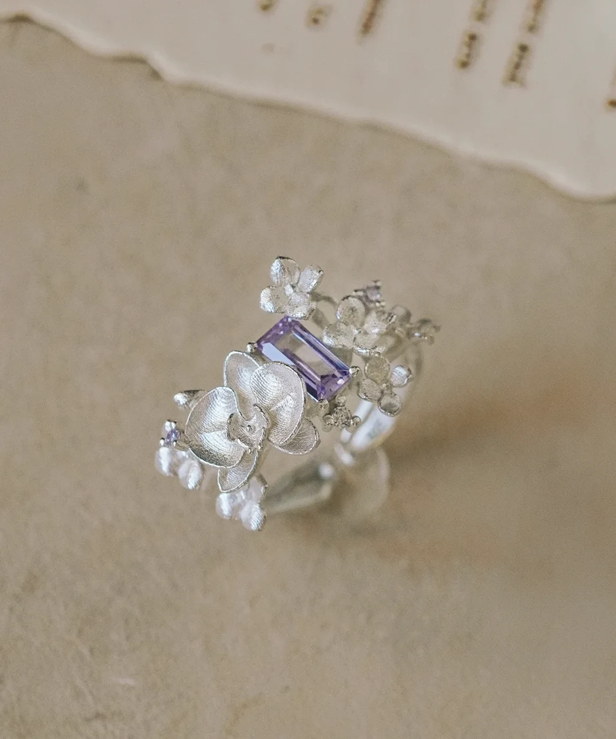 A close-up of the Unique Gemstone Ring, an orchid-inspired S925 silver ring featuring a central purple rectangular-cut gemstone.